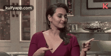 a woman in a red dress is sitting on a couch and pointing at something with her fingers .