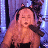 a woman with pink hair is wearing headphones and a cat ear headband in front of a microphone