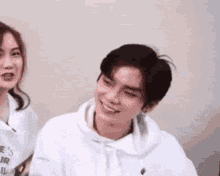 a man in a white hoodie is smiling next to a woman in a white shirt .