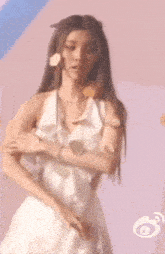 a woman in a white dress with a flower in her hair is standing in front of a pink wall .