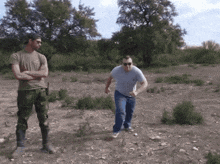 two men are standing in a field with trees in the background and one is wearing sunglasses
