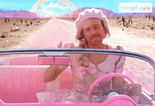 a man in a pink dress is driving a pink car with the misgif.app app on the bottom