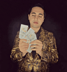 a man in a gold jacket holds a stack of 100 dollar bills in his hands