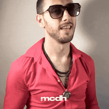 a man wearing sunglasses and a red shirt with mcdh written on the collar