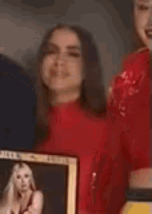a woman in a red shirt is holding a picture of a woman in a frame .
