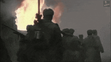a group of soldiers standing in front of a burning building with a russian logo on the bottom left corner