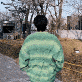 a person wearing a green sweater walking down a sidewalk