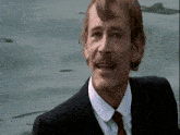 a man with a mustache wearing a suit and tie is standing in front of a body of water