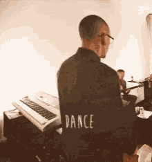 a man in a black jacket with the word dance on the back is playing a piano .