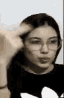 a woman wearing glasses and a black shirt is making a face .