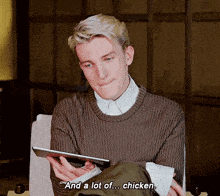 a man is sitting in a chair holding a tablet and saying and a lot of ... chicken .