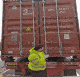 a man in a yellow jacket is pointing at a red triton container