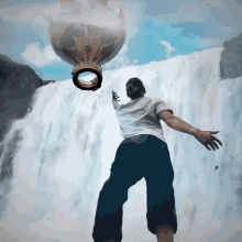 a man standing in front of a waterfall with a hot air balloon flying overhead