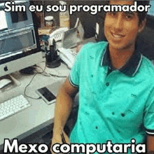 a man in a blue shirt is sitting at a desk with a computer .