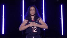 a woman wearing a uconn basketball jersey holds her fist in the air