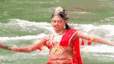 a woman in a red and gold dress is dancing in front of a river .