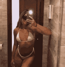 a woman in a bikini is taking a selfie in a bathroom mirror