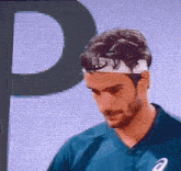 a man wearing a headband and a blue shirt with the letter p in the background