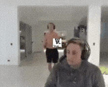 a man wearing headphones is standing in front of a man without a shirt in a living room .