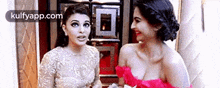 two women in dresses are standing next to each other and talking .
