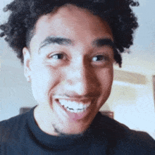 a man with curly hair and a tattoo on his arm smiles