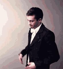 a man in a tuxedo and bow tie is standing in front of a white wall .