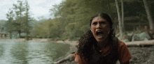 a woman is sitting on the shore of a lake screaming .