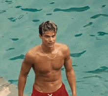 a shirtless man in red shorts is standing in a pool