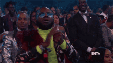 a man wearing sunglasses and a neon green turtleneck is clapping in a crowd at a bet show