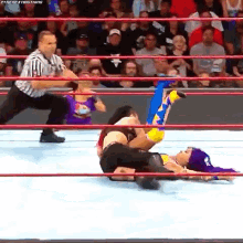 two women are wrestling in a wrestling ring with a referee watching .