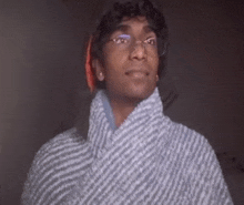 a man wearing glasses and a hat is wrapped in a blanket and looking up .