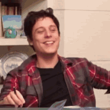 a man wearing a plaid shirt is smiling and holding a pen