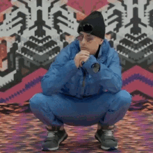 a man in a blue jacket is squatting down in front of a colorful wall .