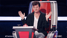 a man is sitting in a chair with his hands in the air and a nbc logo in the corner