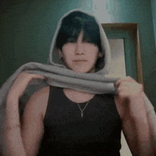 a man wearing a black tank top and a necklace is holding a gray scarf around his neck .