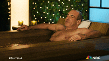 a shirtless man is laying in a bathtub with the nbc logo on the bottom right