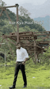 a man in a white shirt and black pants is standing in a grassy field in front of a wooden structure .