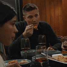 a man is eating a piece of food while sitting at a table with wine glasses