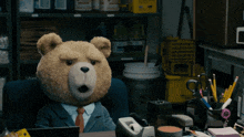 a teddy bear in a suit sits at a desk