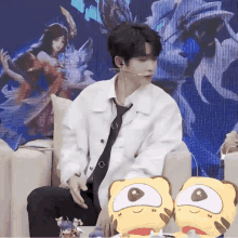 a man in a white jacket and tie is sitting on a couch with stuffed animals in front of him