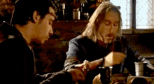 two men are sitting at a table with food and drinks .