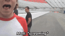 a man is screaming on a race track while another man stands behind him .