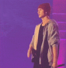 a man wearing a red beanie and a gray jacket is standing on a stage holding a microphone .