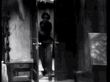 a black and white photo of a man standing in a doorway .