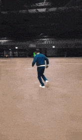 a man in a blue jacket and black pants is running in an empty arena