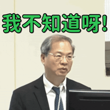 a man in a suit and tie stands in front of a computer monitor with chinese writing on the bottom