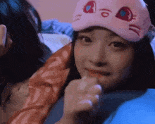 a woman wearing a pink sleep mask is sitting on a bed .
