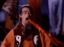 a man with a beard and long hair is wearing a red robe with a yin yang symbol on it and eating something .