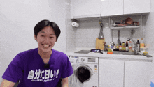 a man wearing a purple shirt that says gokisen factory smiles in a kitchen