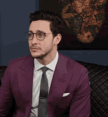 a man in a purple suit and tie is sitting on a black couch
